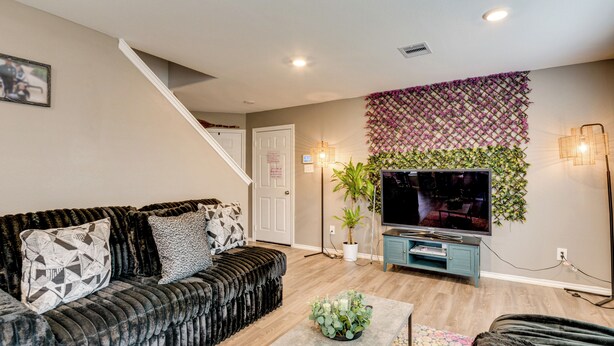 A living room with a black sofa, a coffee table, a TV, and a staircase. - 2 Mi to Historic Dtwn Magnolia: Family Retreat (Magnolia)