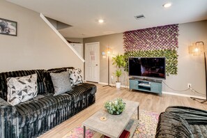 A living room with a black sofa, a coffee table, a TV, and a staircase. - 2 Mi to Historic Dtwn Magnolia: Family Retreat (Magnolia)