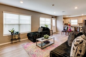 A living room with a sofa, a coffee table, and a TV. There is a kitchen in the background with a refrigerator and a sink. - 2 Mi to Historic Dtwn Magnolia: Family Retreat (Magnolia)