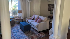 Una sala de estar con un sofá color beige, un reposapiés azul, alfombra estampada y una puerta blanca.