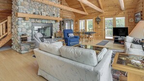 A cozy cabin interior with a stone fireplace, wooden beams, a sofa, a blue armchair, and a television.