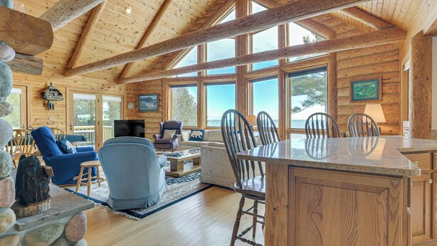 A spacious living area with a wooden ceiling, large windows, and a stone fireplace.