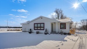Une maison de plain-pied avec un toit à pignon, un porche à l’avant et une allée recouverte de neige.