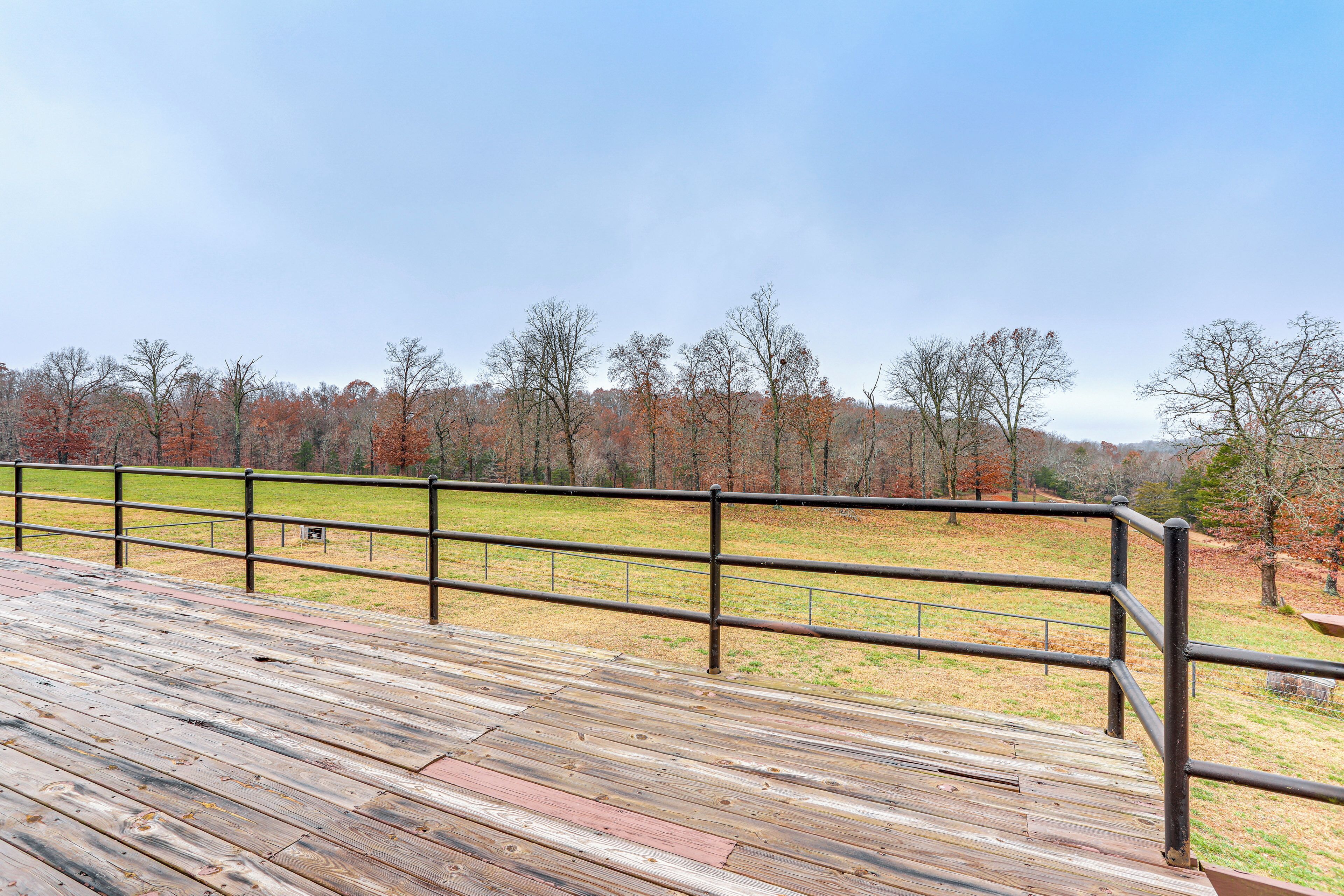 Une terrasse en bois avec une rambarde en métal, donnant sur un champ verdoyant et des arbres.