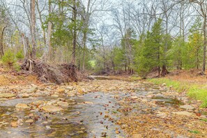 A natural landscape with a clear stream, surrounded by trees and rocky terrain.