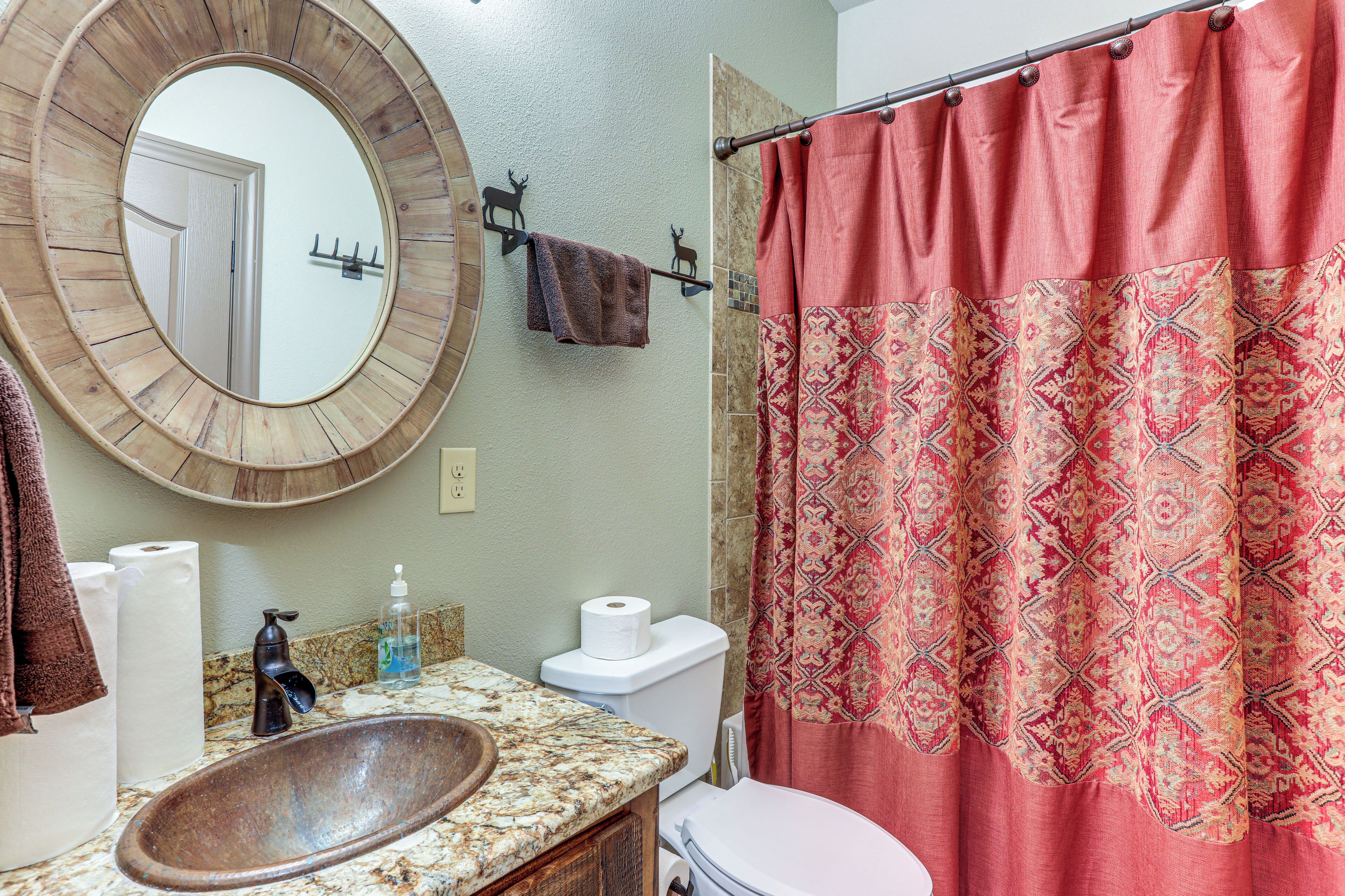 A bathroom with a wooden sink, a round mirror, a toilet, and a red patterned shower curtain.