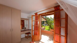 A bedroom with a bed, a desk, and a wardrobe. There is a large window with curtains.