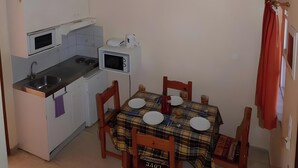 A compact kitchen with a dining table, chairs, and a microwave. - Two-Bedroom Apartment 7 (Roda)