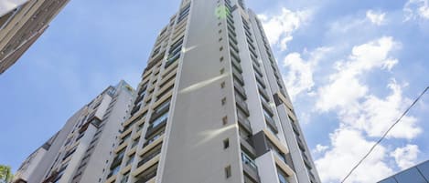 A high-rise building with multiple floors, large windows, and a clear sky with clouds.