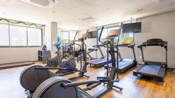 Un gimnasio con diferentes máquinas de cardio, una televisión y amplias ventanas.