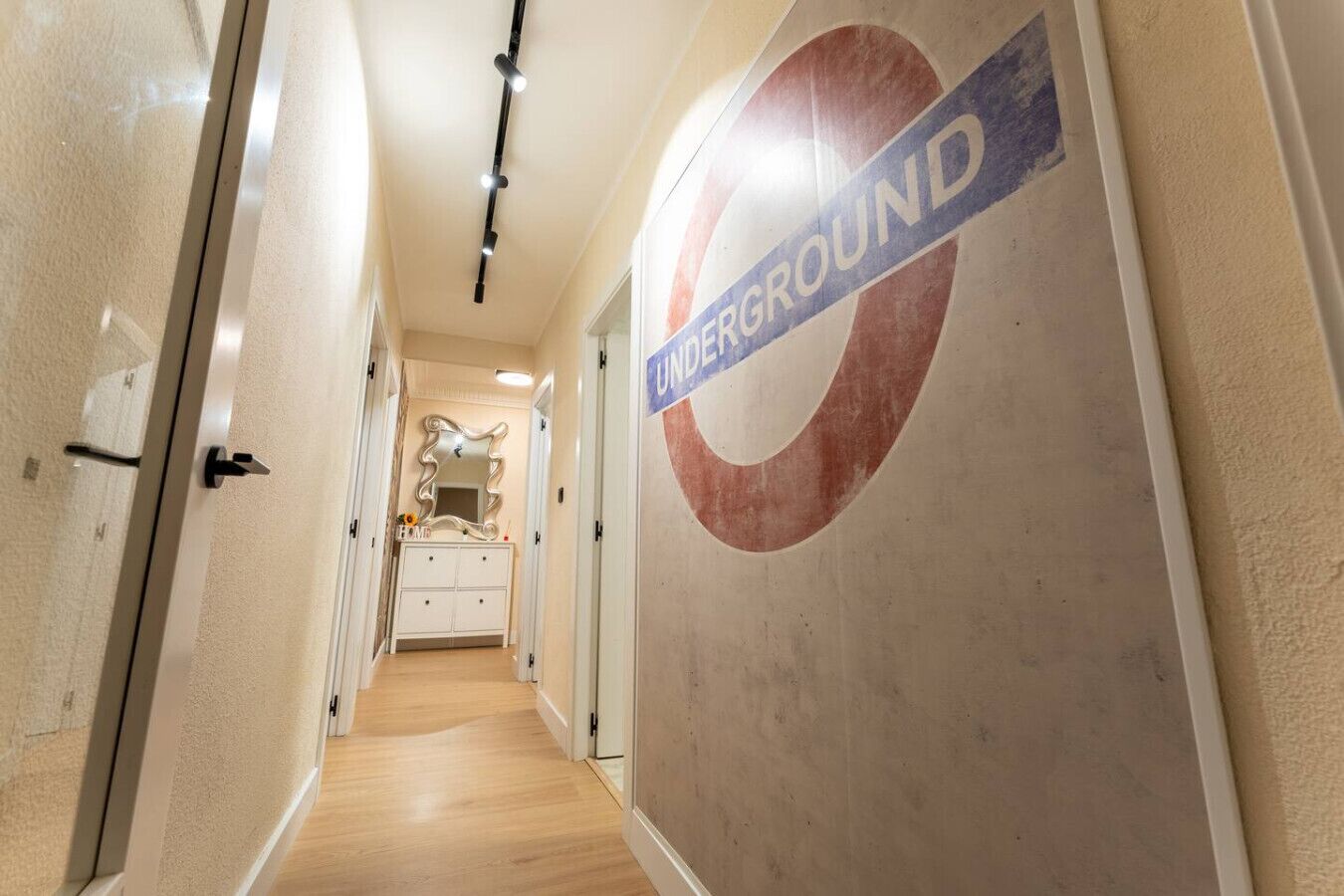 Een gang met een muur waarop het logo van de London Underground staat, een witte wastafel met spiegel en een houten vloer.