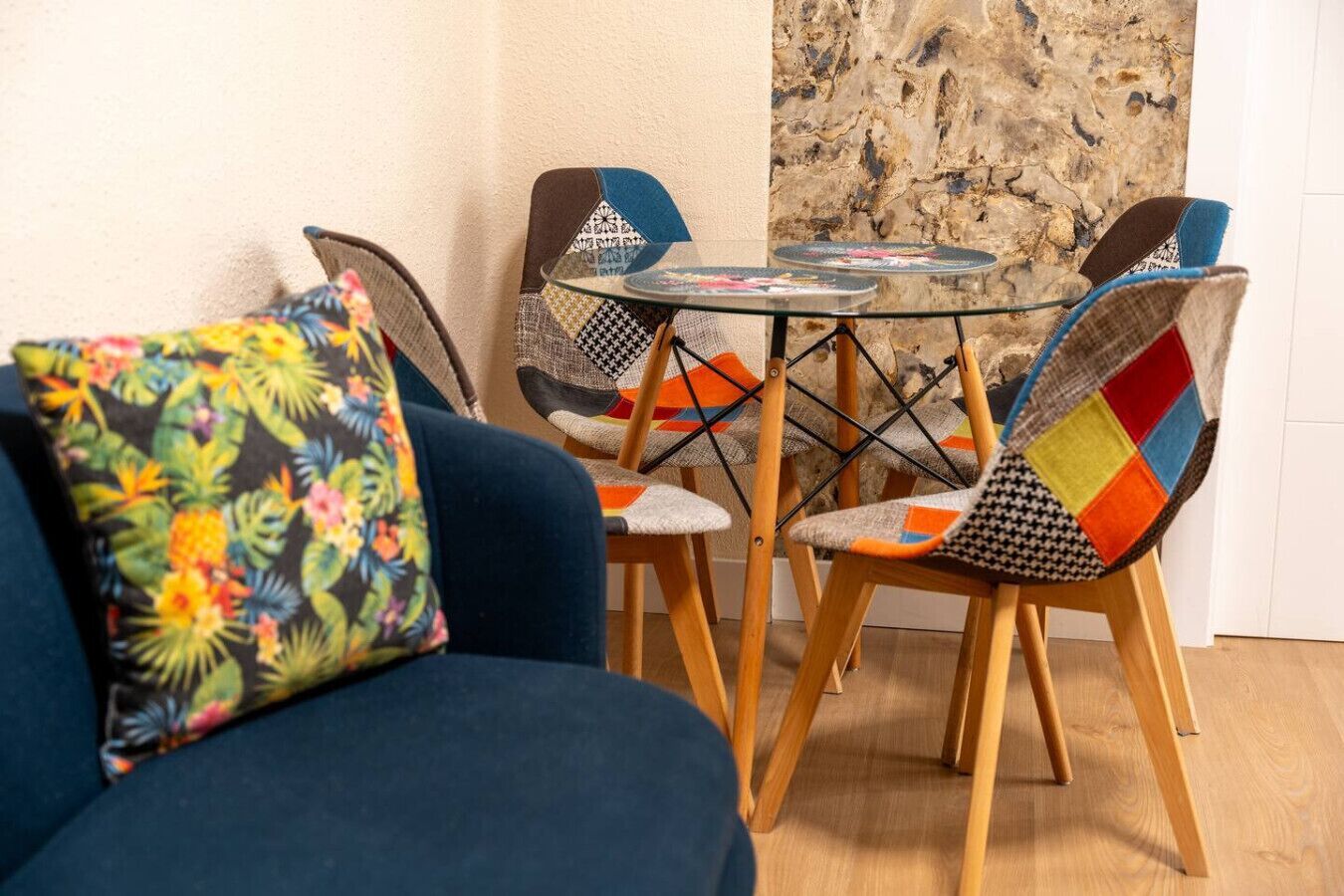 Een klein eetgedeelte met een glazen tafel en stoelen met kleurrijke bekleding.