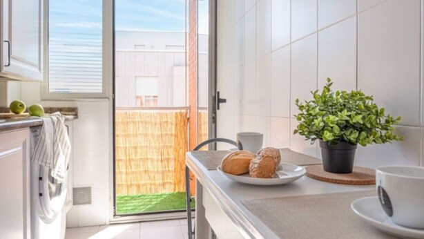 A modern kitchen with a sliding glass door leading to a balcony, a potted plant, and a plate with bread on the counter. - San Roman apartment with private parking (Santander)