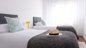 A hotel room with two beds, a hat on the bed, and a window with sheer curtains. - San Roman apartment with private parking (Santander)