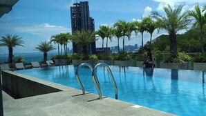 A swimming pool with metal railings, surrounded by palm trees and a cityscape in the background. - Peaceful SEA View Condo (Pattaya)
