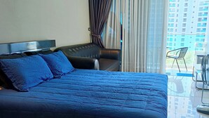 A hotel room with a large bed, a flat-screen TV, a ceiling fan, and a view of a building through the window. - Peaceful SEA View Condo (Pattaya)