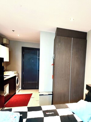 A hotel room with a bed, a desk with a chair, a washing machine, a wardrobe, and a door to the outside. - Peaceful SEA View Condo (Pattaya)