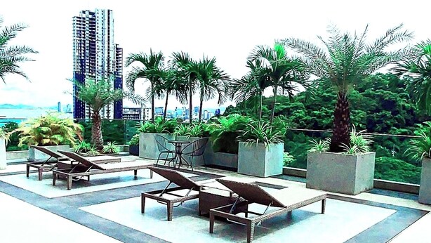 An outdoor seating area with lounge chairs and planters, surrounded by greenery and a cityscape in the background. - Peaceful SEA View Condo (Pattaya)