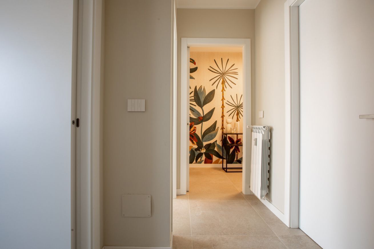 A hallway with a tiled floor, a radiator on the right, and a wall with a tropical plant mural.