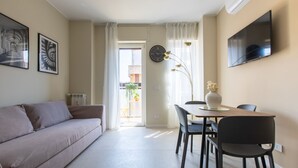 Un salon moderne avec un canapé, une table à manger, des chaises et un téléviseur. Il y a une fenêtre avec des rideaux et une vue sur l’extérieur.