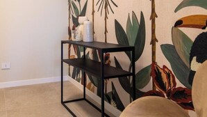 Une pièce avec une étagère en métal noir, un mur orné d’un motif de feuilles tropicales et une chaise.