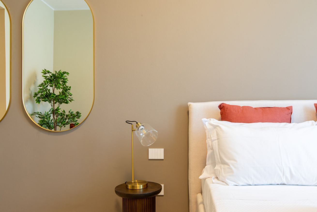 A bedroom with a bed, a bedside lamp, a wall-mounted mirror, and a small potted plant.