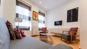 Un soggiorno moderno con un divano grigio, una sedia in legno, un tavolino e una TV a parete.
