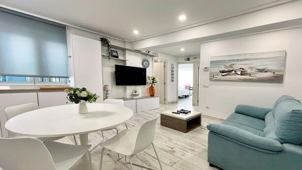 A modern living room with a round white table, white chairs, a blue sofa, and a painting on the wall. - 3 rooms apartment close beach (Santander)