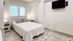 A bedroom with a bed, bedside tables, a TV mounted on the wall, and a window with blinds. - 3 rooms apartment close beach (Santander)
