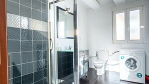 Een moderne badkamer met een glazen douchecabine, een toilet, een wasmachine en een wastafel met een spiegel erboven.