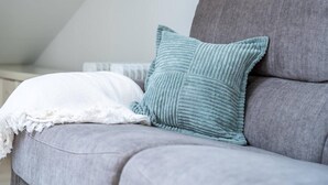 Een grijze bank met een witte plaid en een turquoise kussen.