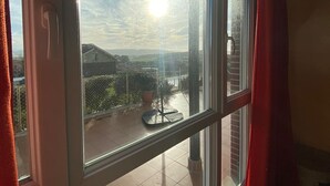 Una stanza con una grande finestra che si affaccia su un balcone con una pianta in vaso e un supporto in metallo.