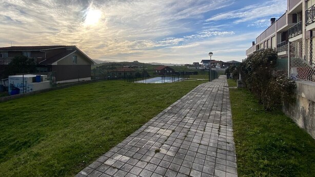 Un vialetto lastricato conduce a un edificio con piscina, immerso nel verde sotto un cielo nuvoloso.
