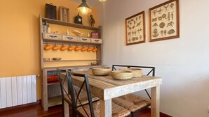 Zona pranzo con tavolo in legno, sedie in vimini e ripiano con tazze arancioni.