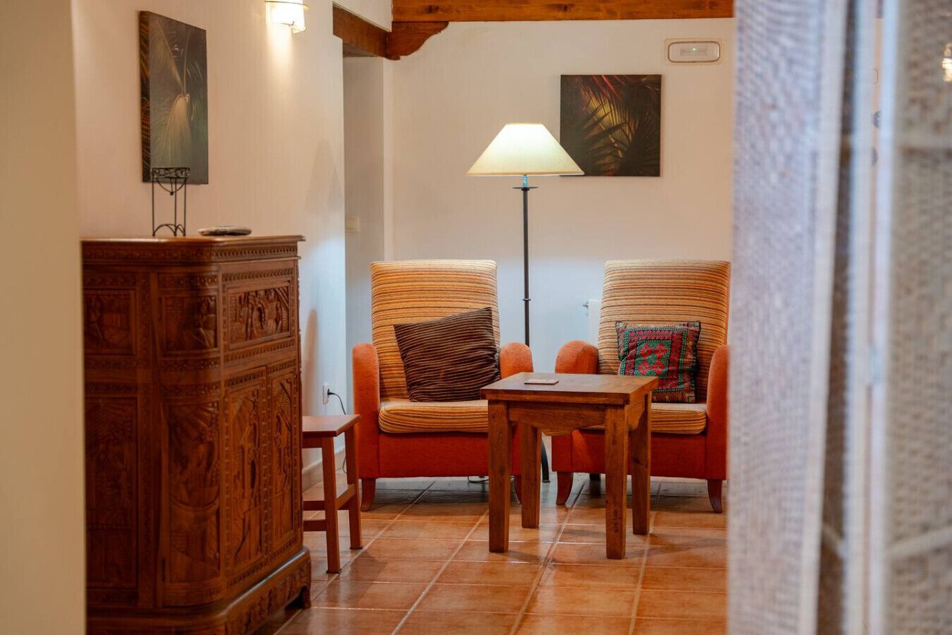 Een gezellige kamer met een houten kast, twee comfortabele fauteuils, een tafeltje en een vloerlamp.
