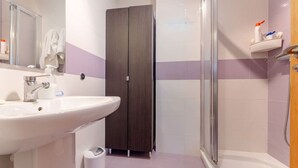 Un bagno con lavandino bianco, armadio in legno scuro e cabina doccia in vetro.