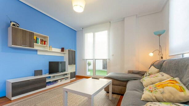 Un soggiorno moderno con una parete blu, un divano grigio, un tavolino da caffè bianco e una TV su un mobile in legno.