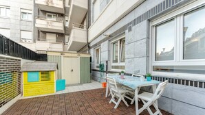Un patio con tavolo e sedie, una piccola area giochi e vista su un edificio con balconi.