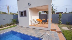 A modern outdoor pool area with a small patio, a single lounge chair, and a table. - The Oasis Airport Pick up Wifi Central (Accra)