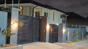 A modern house with a dark exterior, a visible staircase, and a gated entrance. - The Oasis Airport Pick up Wifi Central (Accra)