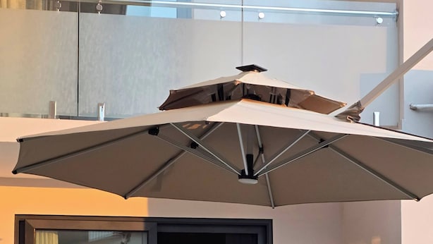 A modern outdoor dining area with a table and chairs, a large umbrella, and a view of the city through a glass door. - The Oasis Airport Pick up Wifi Central (Accra)