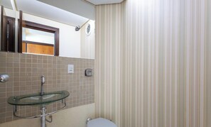 Un baño con lavamanos de vidrio, inodoro y cortina de ducha a rayas.