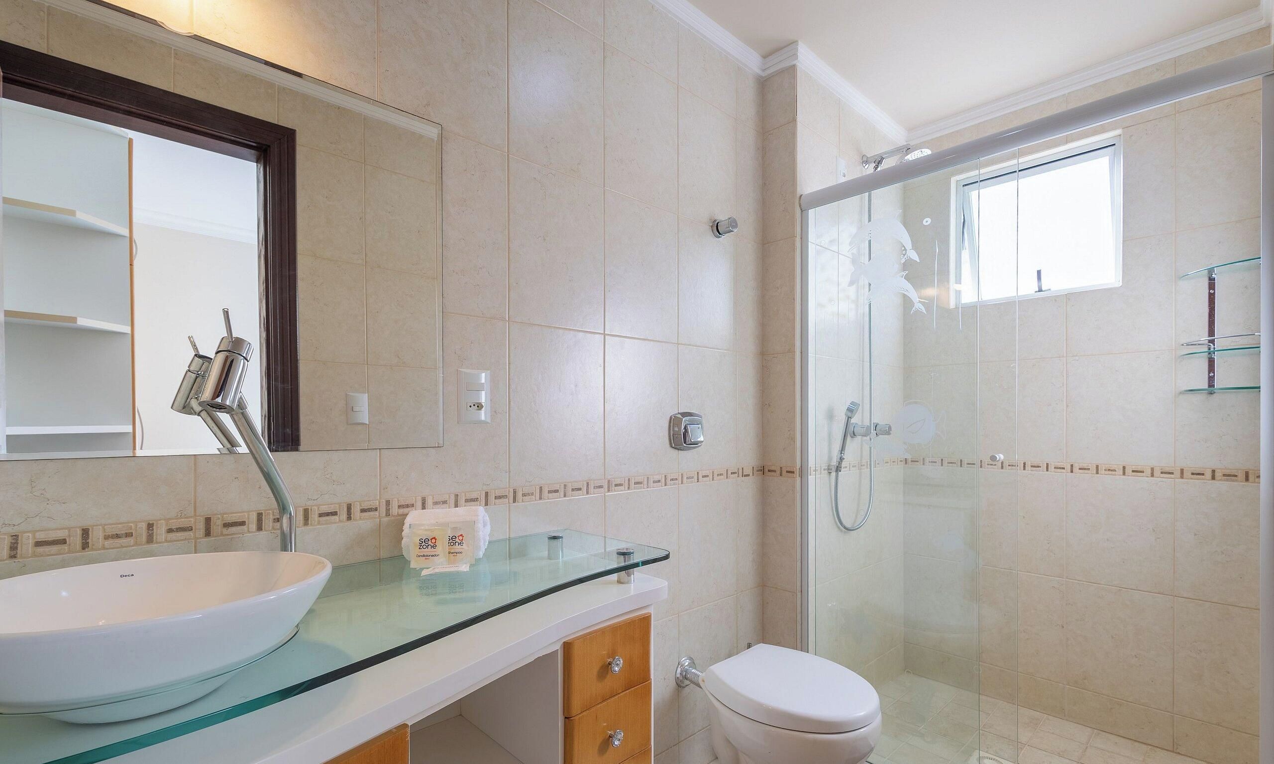 Un baño con lavamanos de vidrio, inodoro, ducha y espejo.