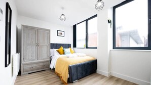 A bedroom with a bed, a wardrobe, and large windows. - Bright Stylish Studio Apartment (Stretford)