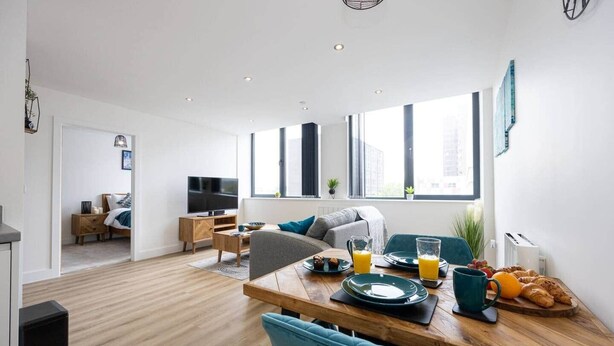 A modern living room with a dining area, a TV, and a large window. - Luxurious Stylish Apartment (Stretford)