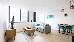 A modern living room with a grey sofa, wooden coffee table, and a dining area with a table and chairs. - Luxurious Stylish Apartment (Stretford)