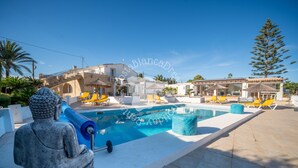 Zona de piscina amb una estàtua de Buda, gandules grogues i un cel blau clar.