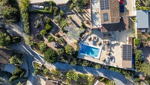 Vista aèria d'una propietat residencial amb piscina, panells solars i un cotxe vermell aparcat al carrer.