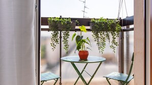 A balcony with a small table and two chairs, a potted plant, and hanging plants. - Daplace - Vico Apartment (Milano)