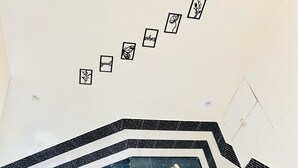 Eine Treppe mit Geländer, gefliestem Boden und einer Wand mit gerahmten Bildern und Schrift.